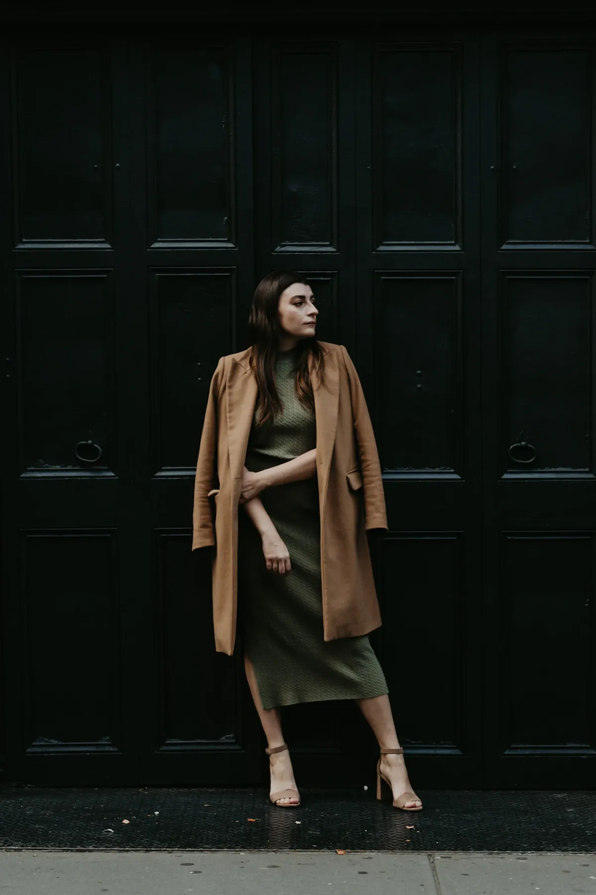 A woman in a brown coat beside a dark wooden door